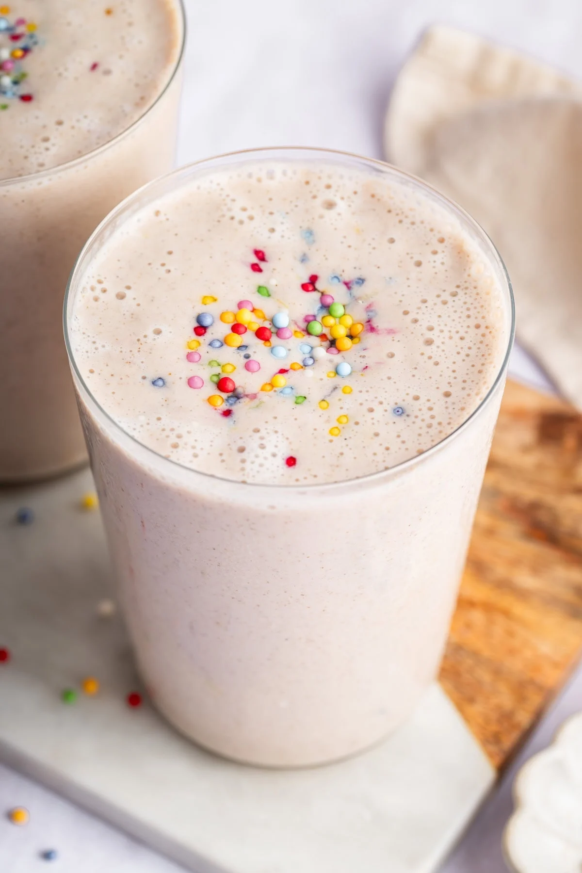 A cake batter protein shake in a glass topped with rainbow sprinkles.
