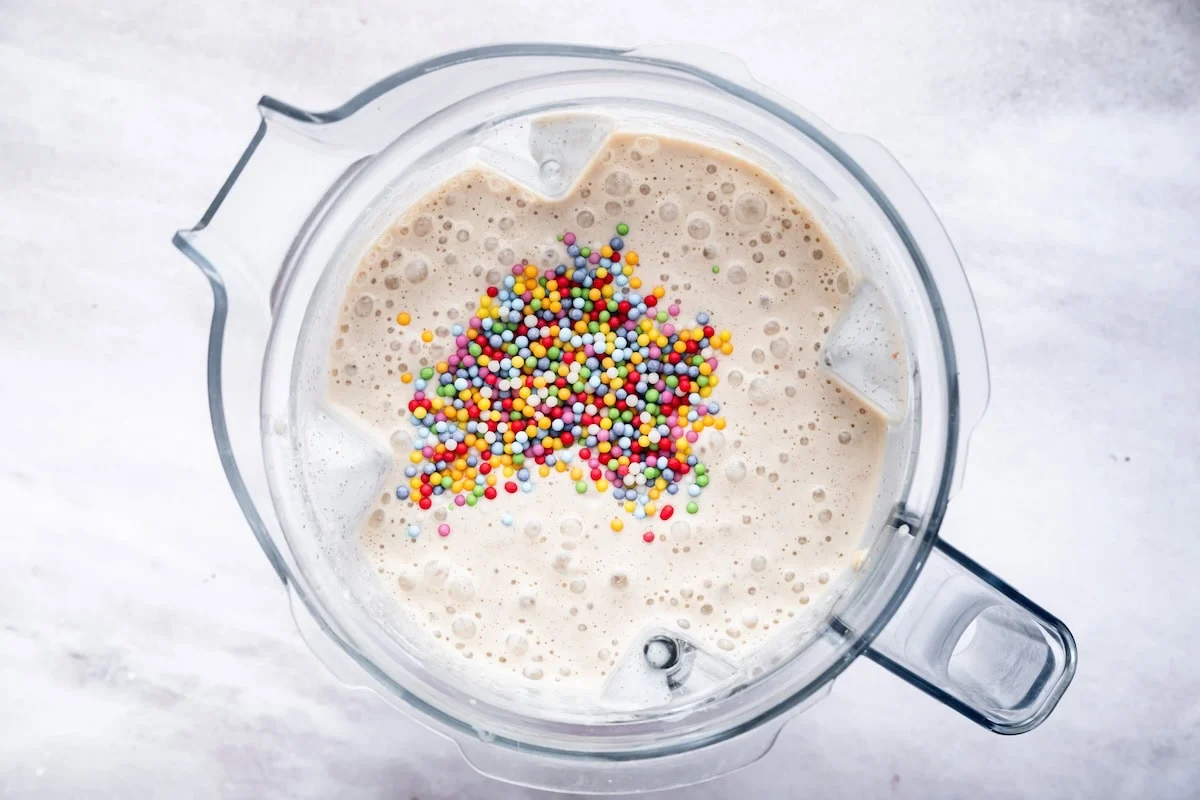 A blended cake batter protein shake in the base of a Vitamix with sprinkles added to it.