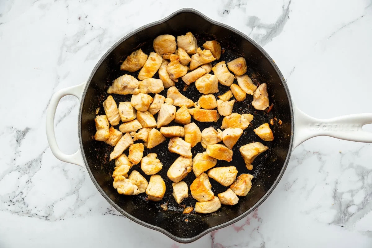 Chicken simmering in a sticky sweet and savory sauce as bourbon chicken thickens in skillet.
