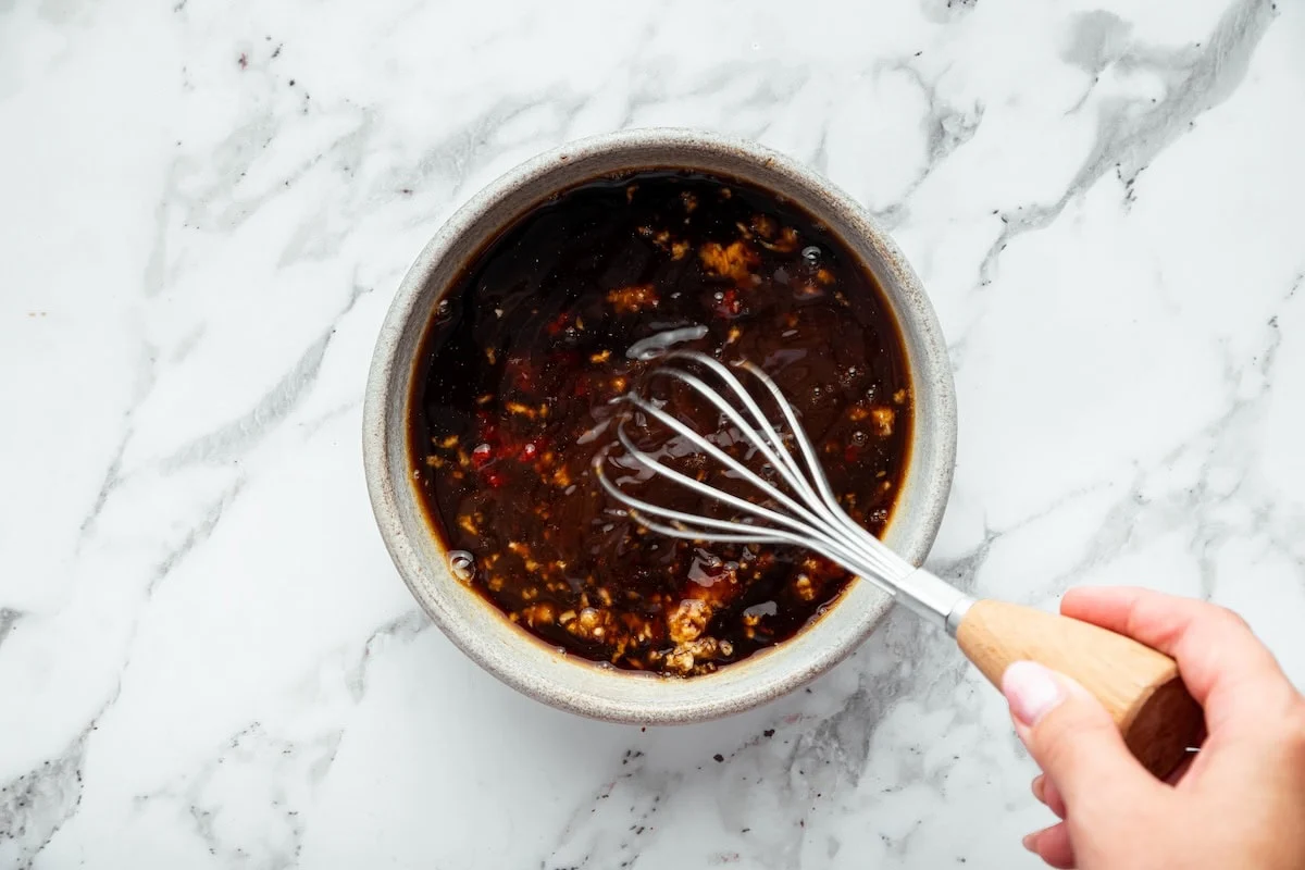Soy-based bourbon chicken sauce being whisked together in a small bowl before cooking.