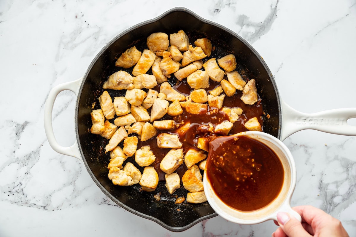 Sweet glazed chicken sauce being poured into skillet over cooked chicken pieces.