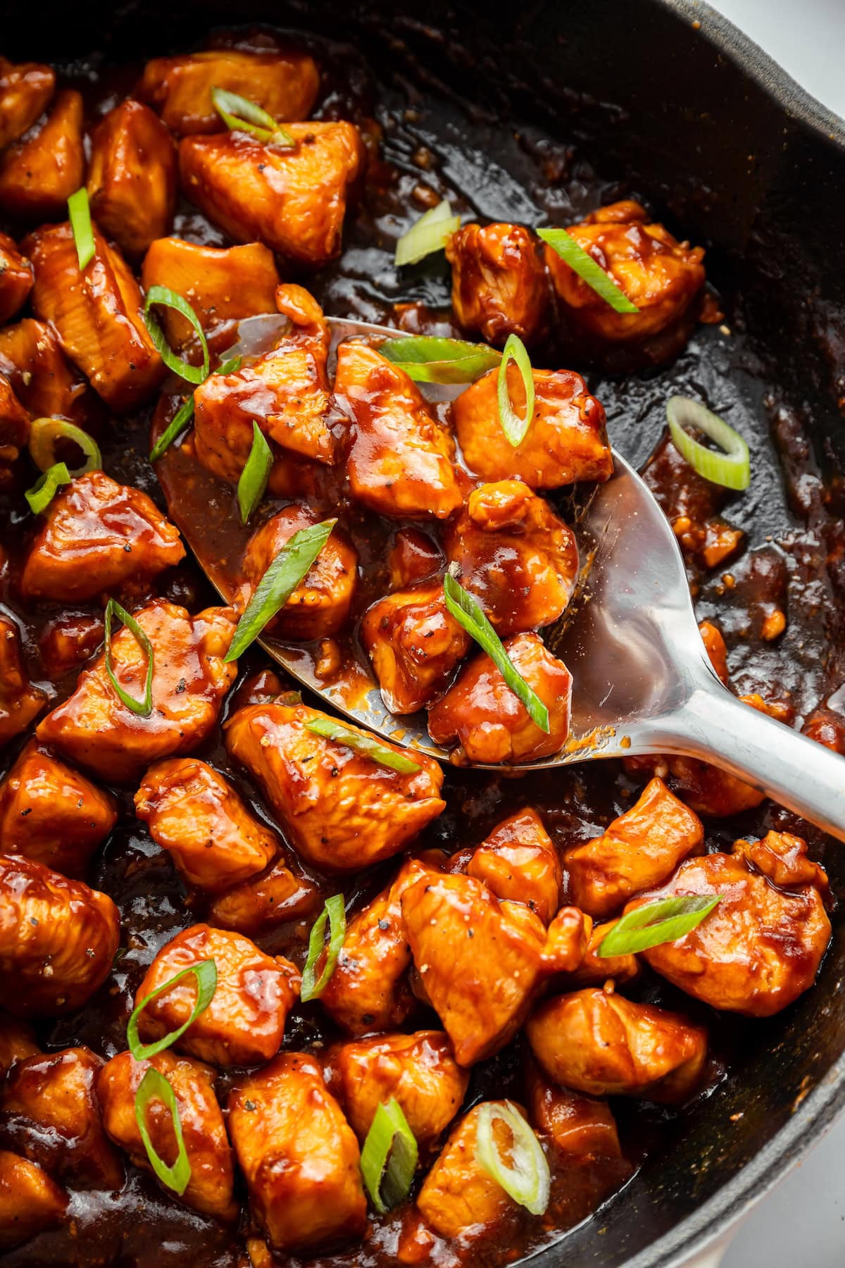Tender glazed chicken being stirred in skillet as the glossy sauce coats each piece.