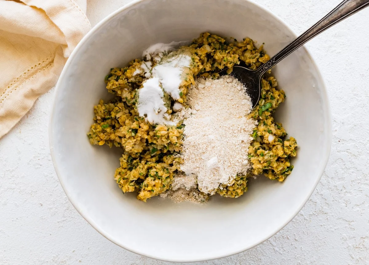 Falafel mixture in bowl with oat flour and baking soda being added.