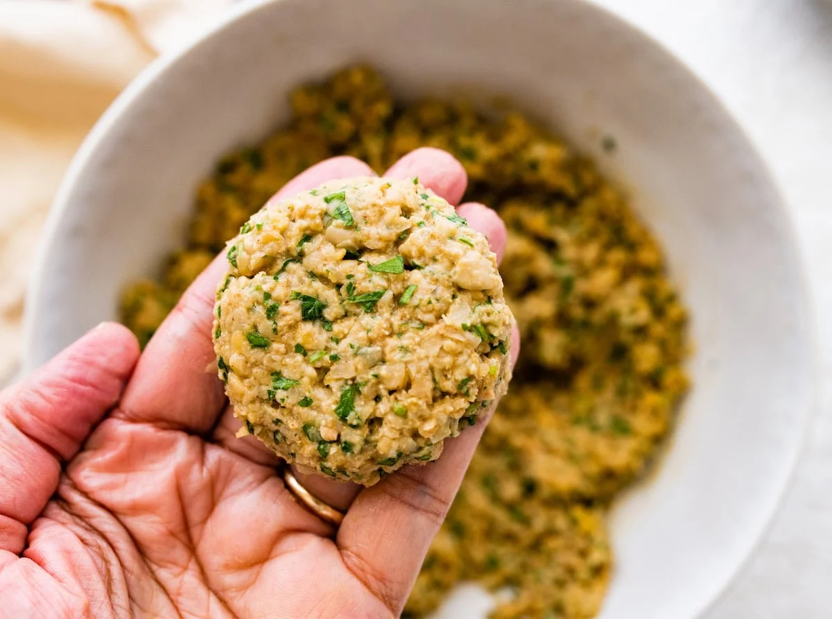Hand holding scoop of falafel mixture ready to shape into patties.
