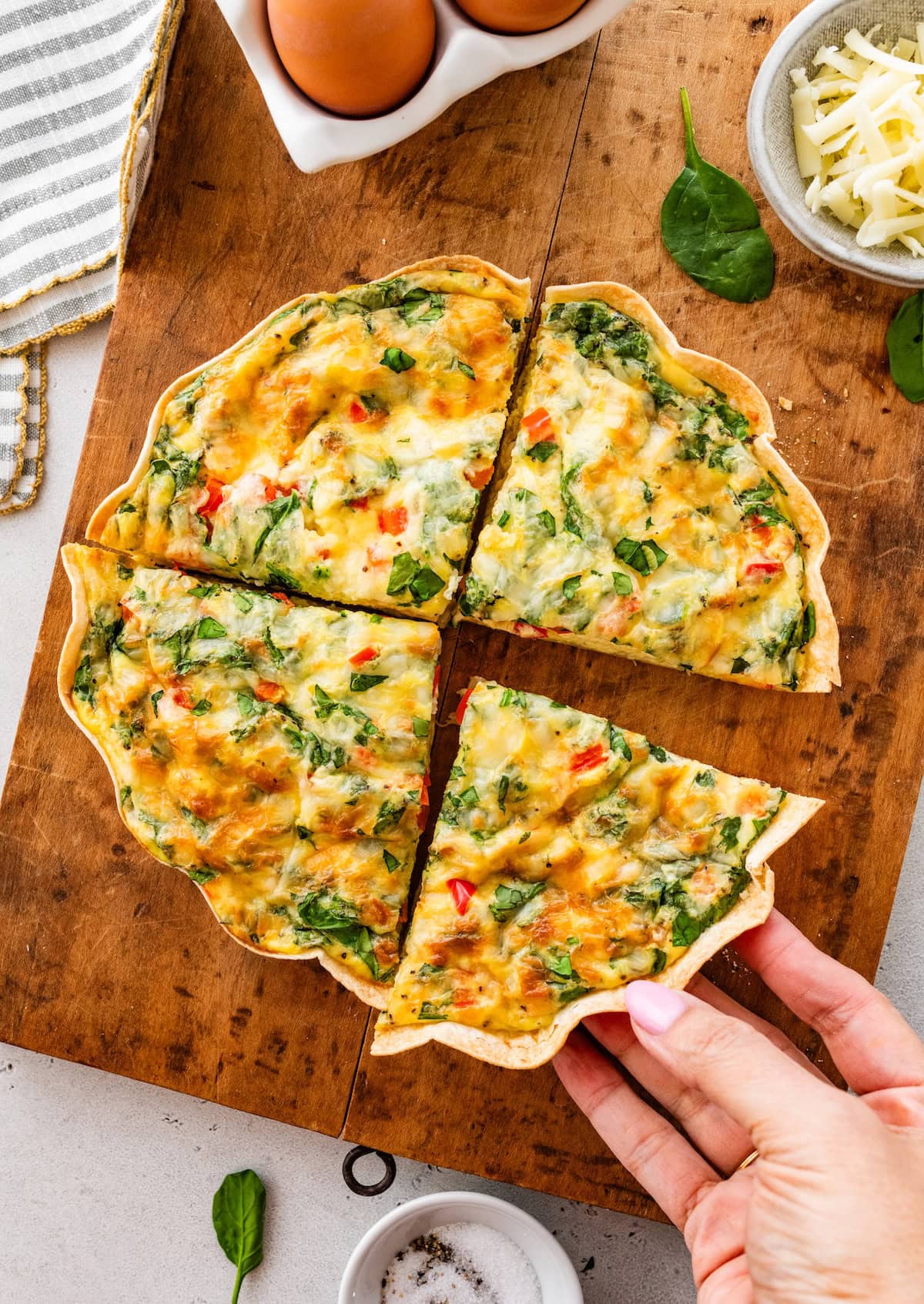 Sliced high-protein tortilla quiche on cutting board with hand lifting one wedge.