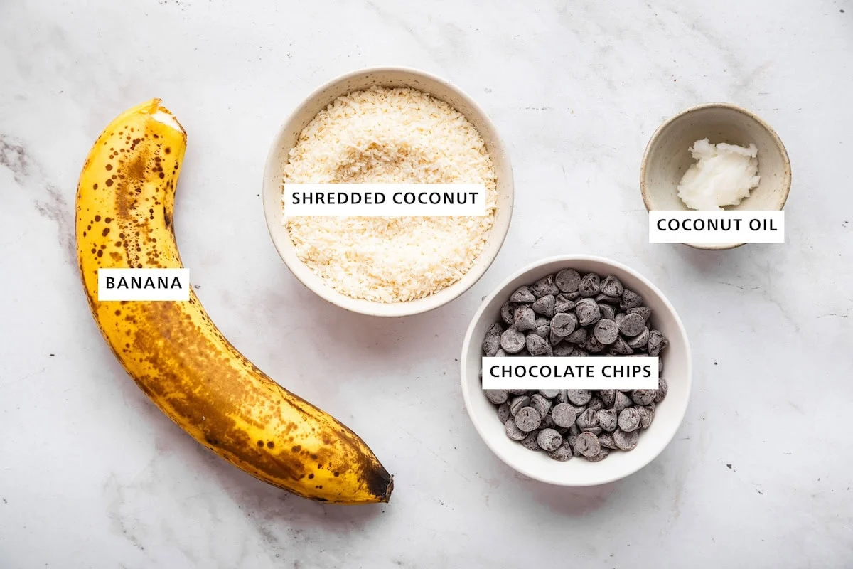 Ingredients used in banana samoas cookies including a banana, shredded coconut, chocolate chips, and coconut oil.