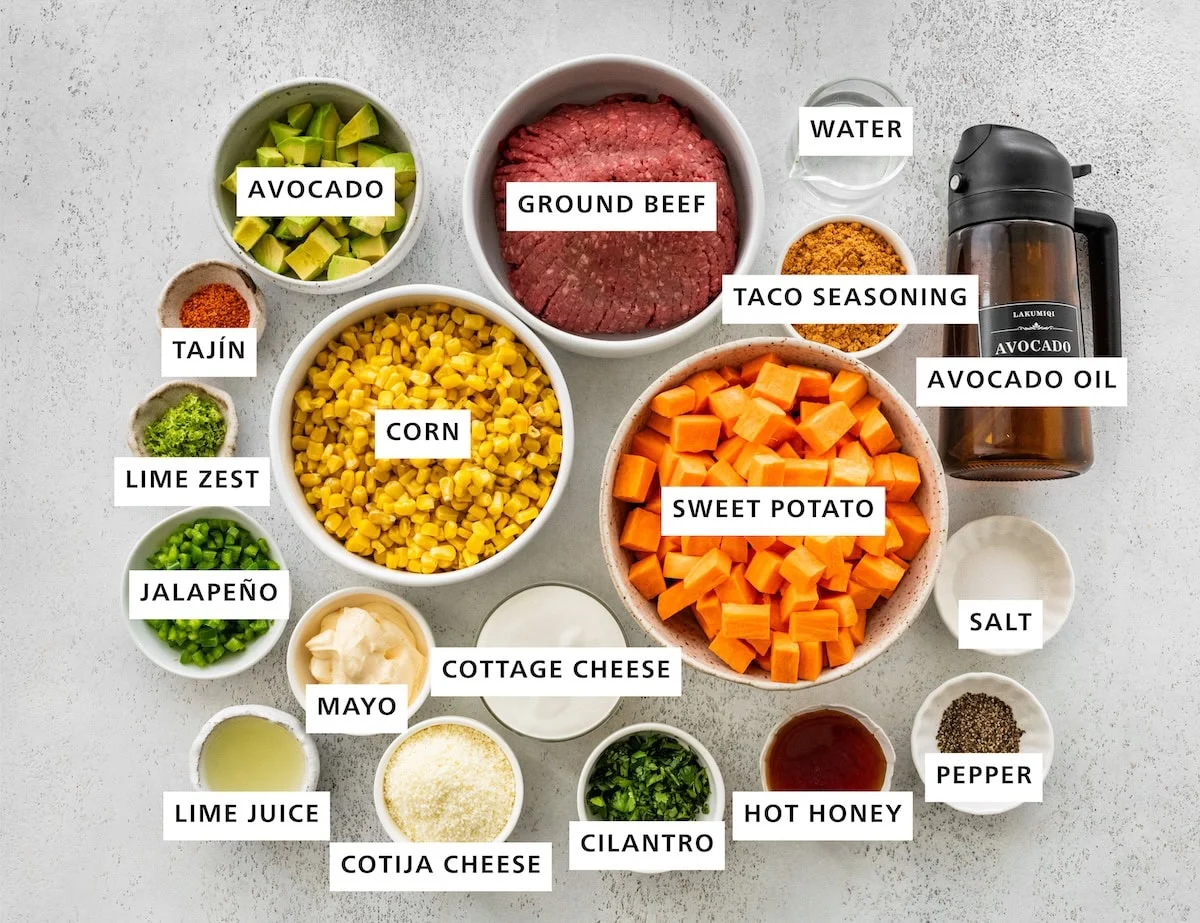 Ingredients used in a street corn sweet potato beef bowl including: ground beef, avocado, corn, sweet potato, avocado oil, taco seasoning, water, salt, pepper, hot honey, cilantro, cottage cheese, cotija cheese, mayo, lime juice, jalapeno, lime zest, and tajin.