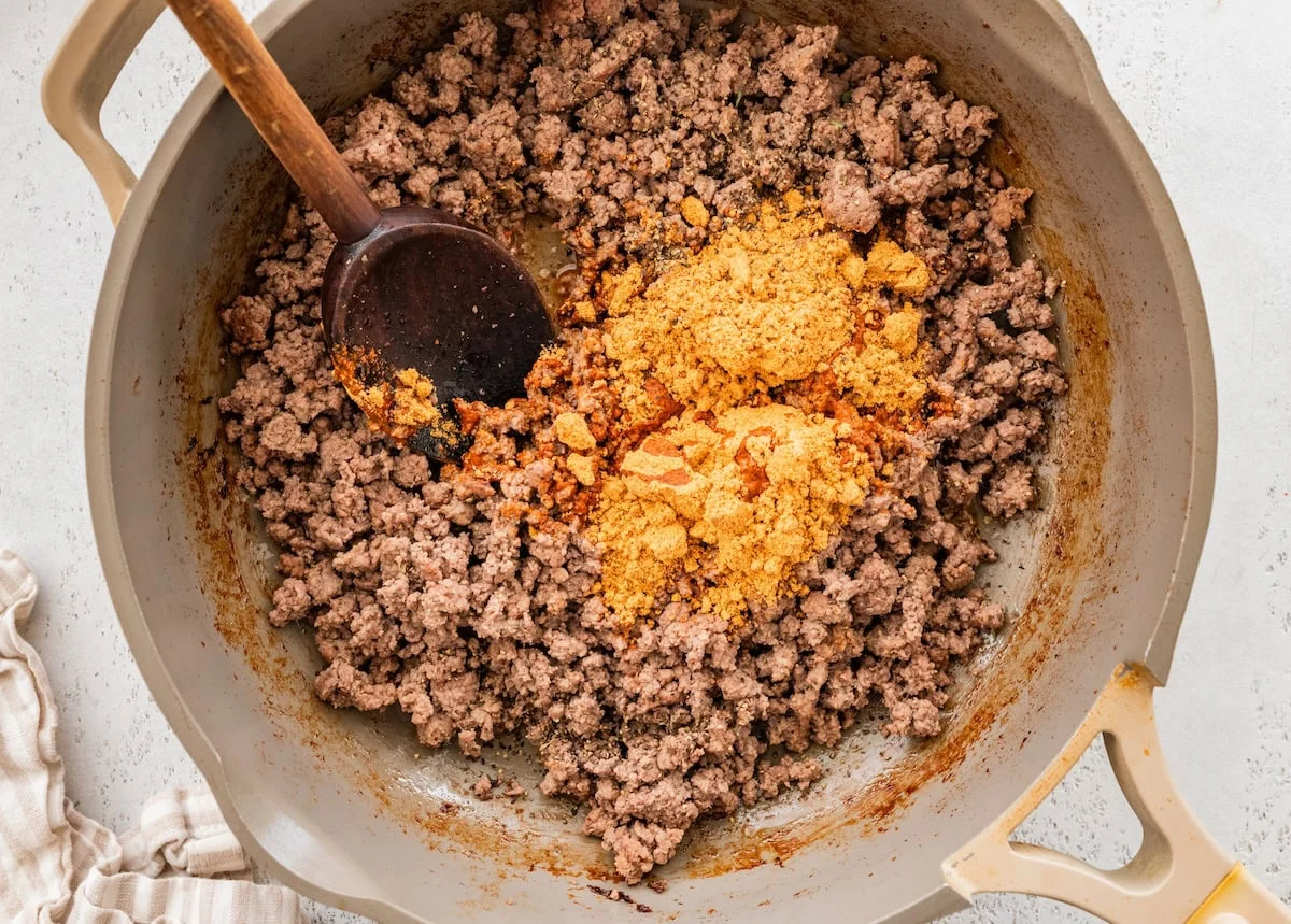 A large skillet with taco seasoning added to cooked ground beef.