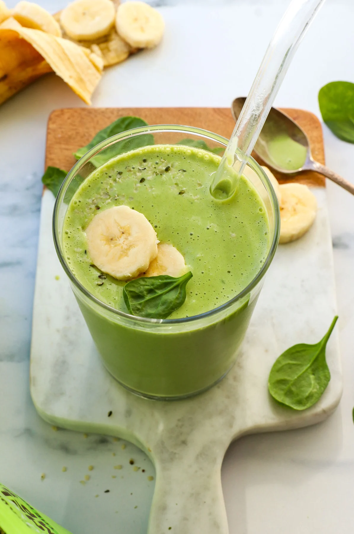 spinach banana smoothie served in a glass with a straw. 