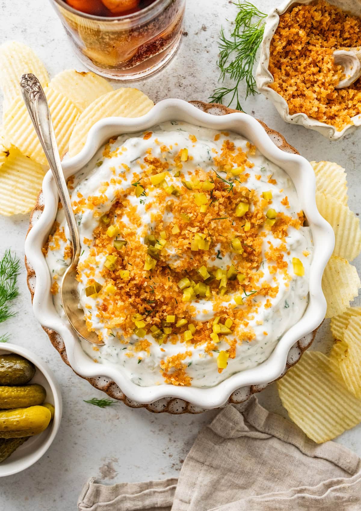 A high protein fried pickle dip in a bowl topped with crispy breadcrumbs and potato chips around the bowl.