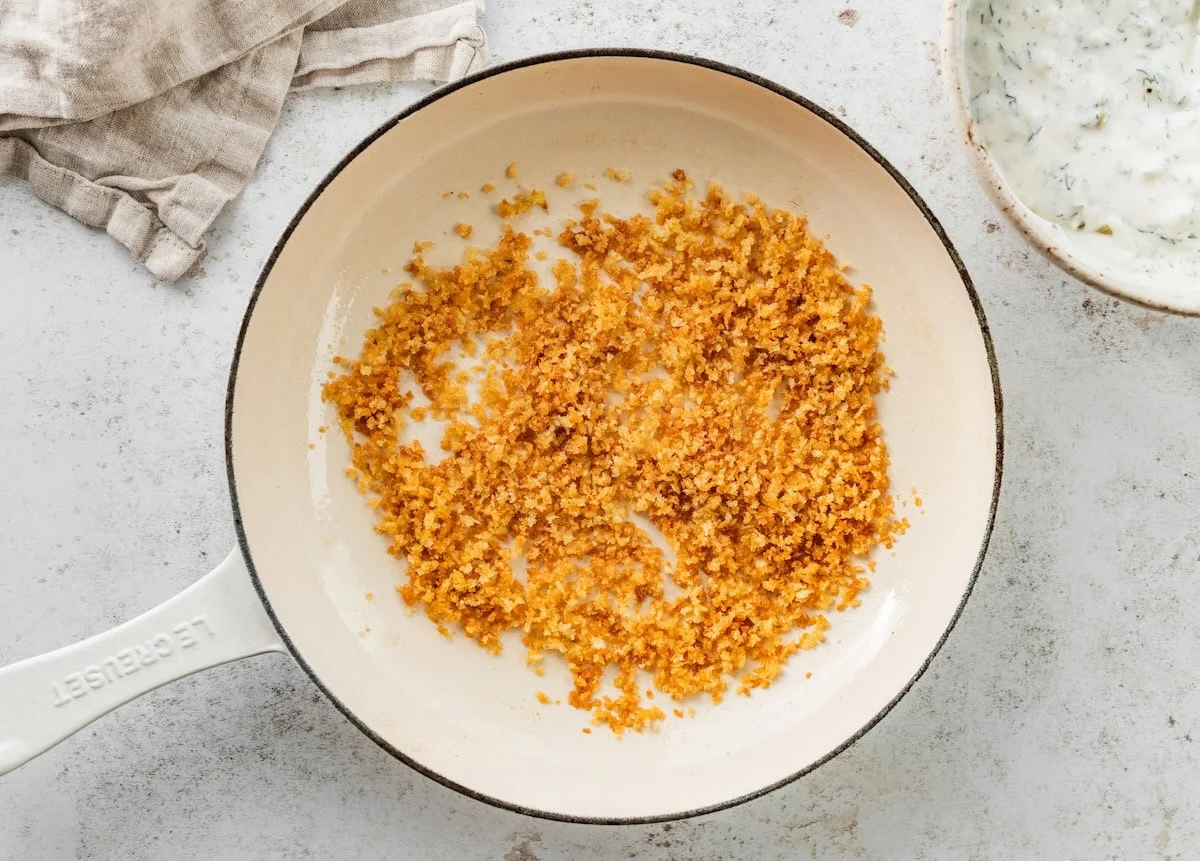 A skillet sauteeing breadcrumbs to a crispy golden color.
