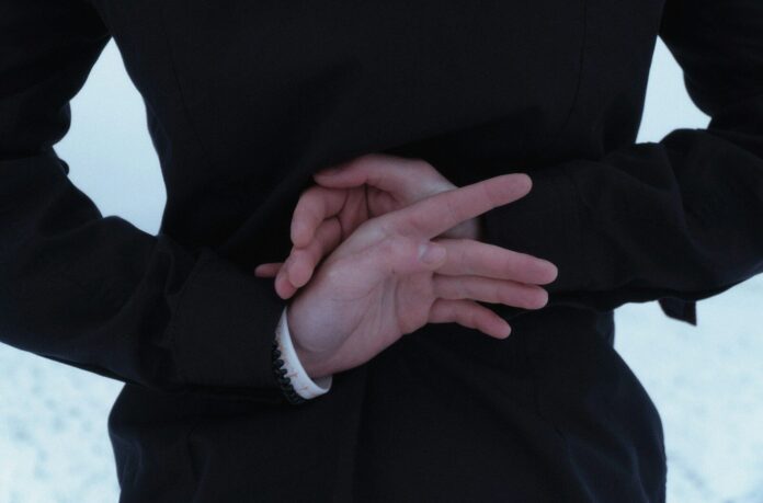 Hands clasped behind a person wearing a dark jacket.